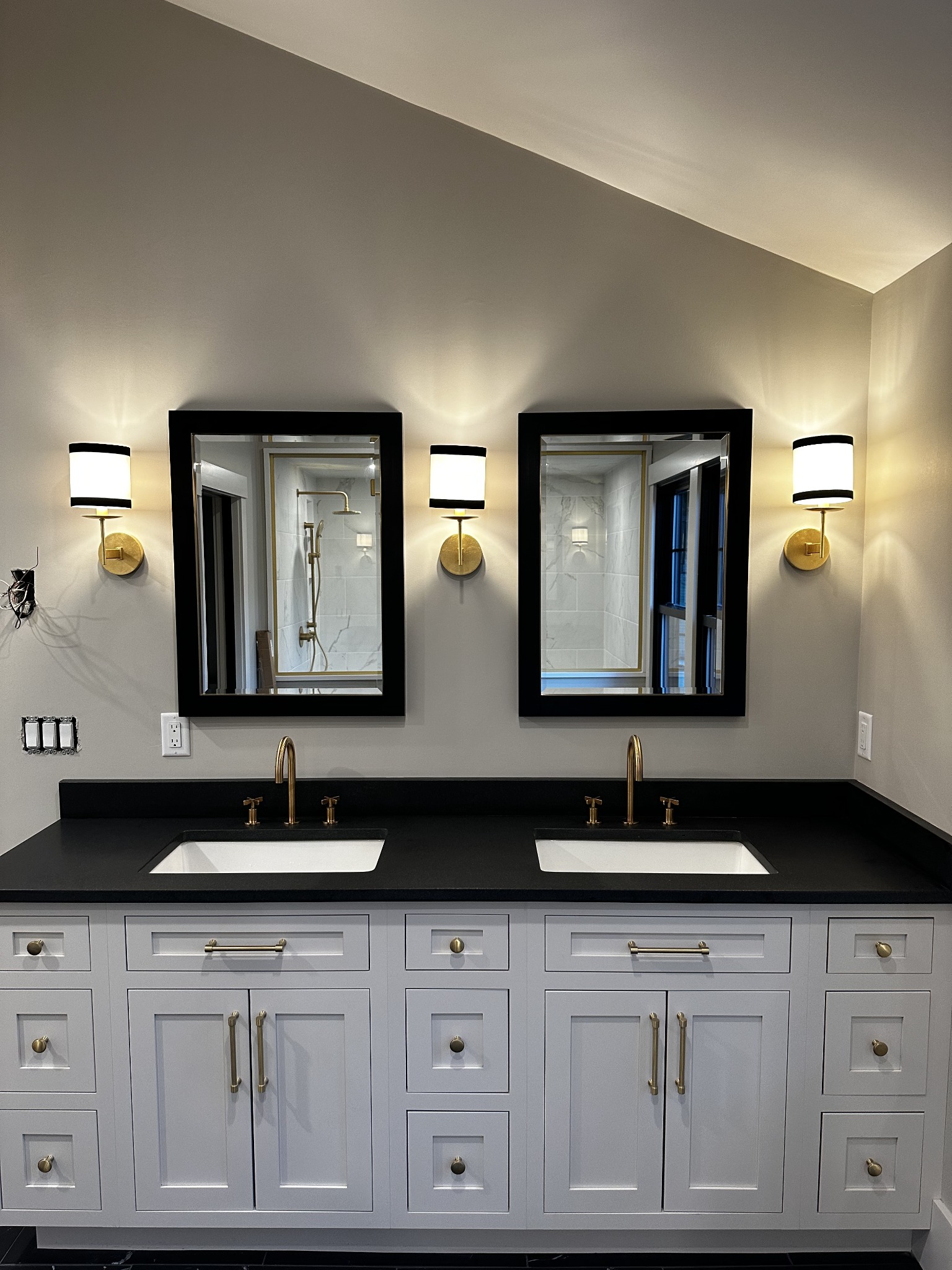 Double bathroom vanity with white cabinetry, a black countertop, brass fixtures, and black-framed mirrors