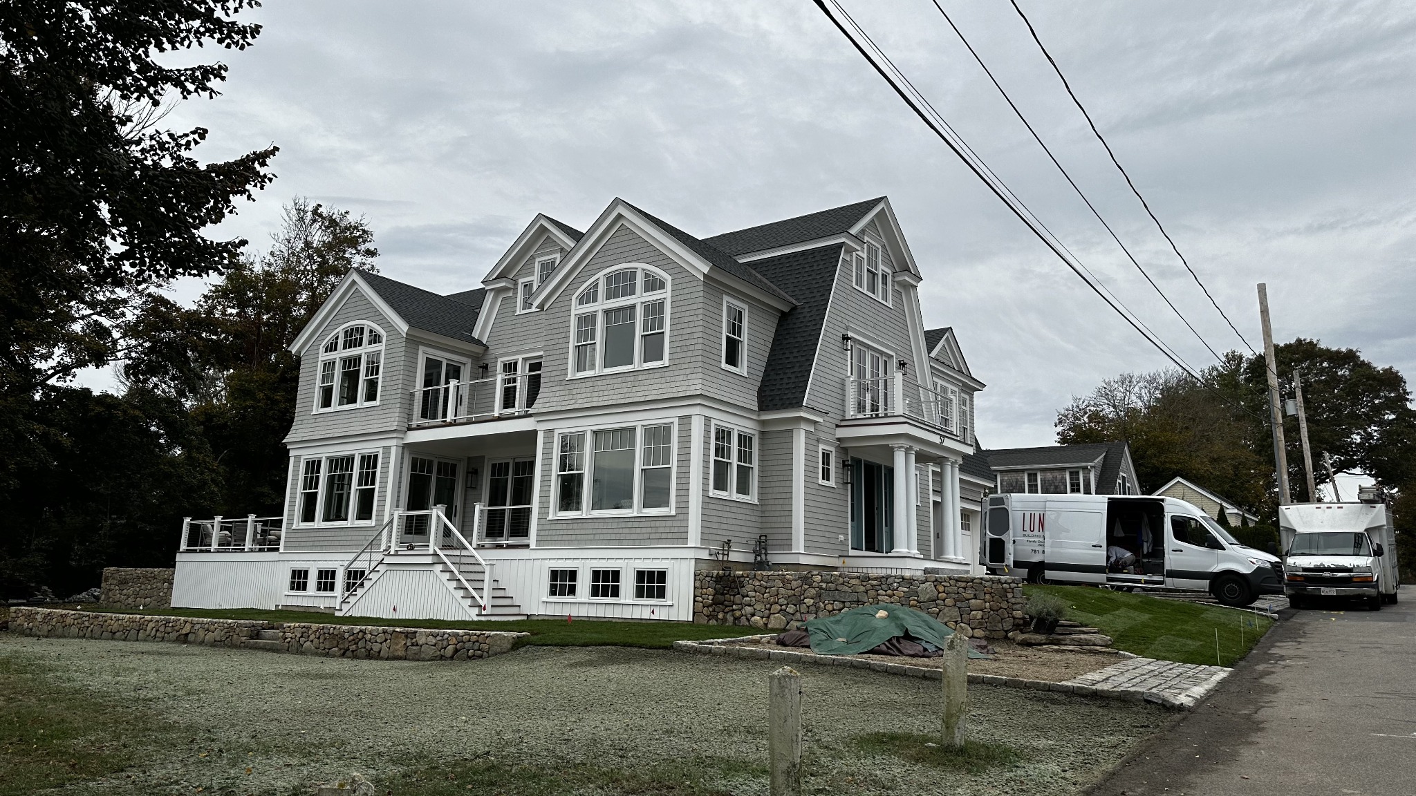 Gray shingle home with large windows, white trim, porches, and stone landscaping