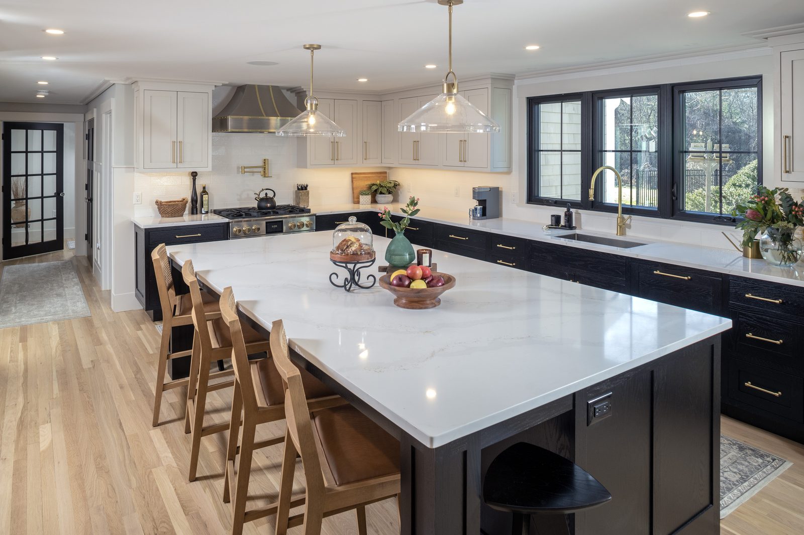 Kitchen with a white island countertop, dark base cabinets, brass hardware, and glass pendant lights