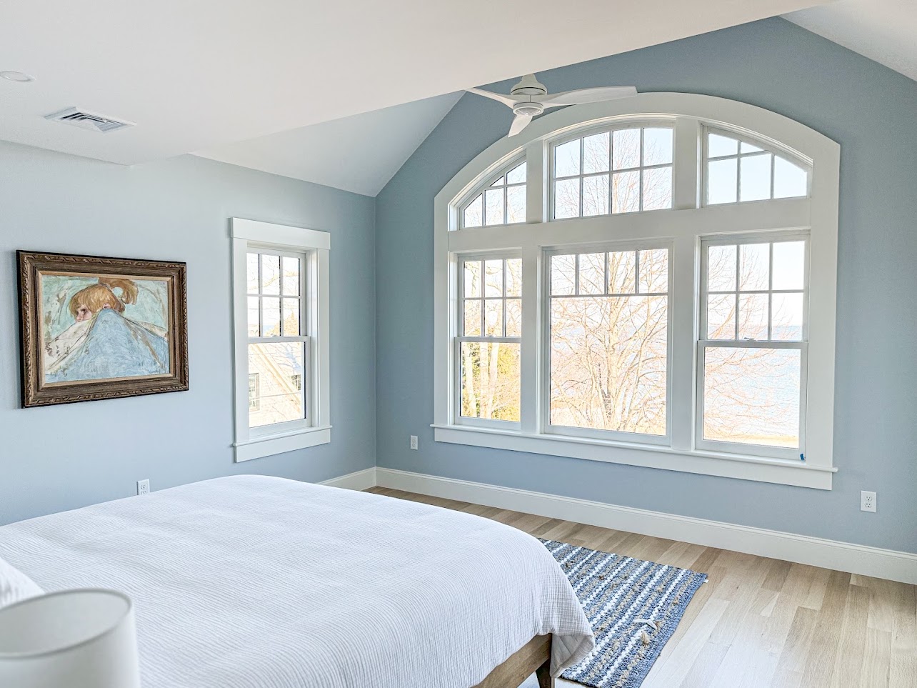 Pale blue bedroom with a vaulted ceiling and arched window overlooking the water